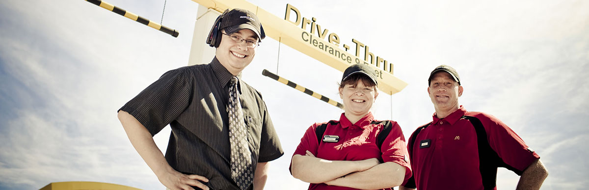 3 McDonalds team members standing near drive-thru entrance sign